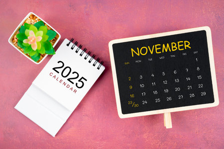 Calendar for November 2025 in black chalkboard on red wooden background.