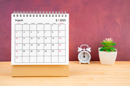 August Monthly desk calendar for 2025 year and alarm clock on wooden table with red background.の写真素材