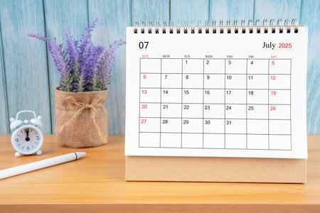July Monthly desk calendar for 2025 year and alarm clock on wooden table.の写真素材