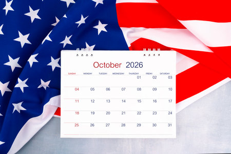 October 2026 desk calendar and United States of America flag on wooden table, Flat lay.