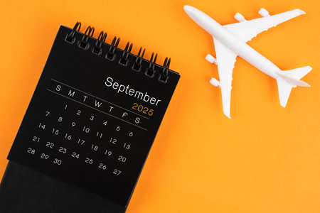 September 2025 black desk calendar and airplane toy on orange color background. Travel concepts.の写真素材
