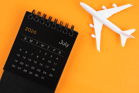 July 2026 black desk calendar and airplane toy on orange background. Travel concepts.