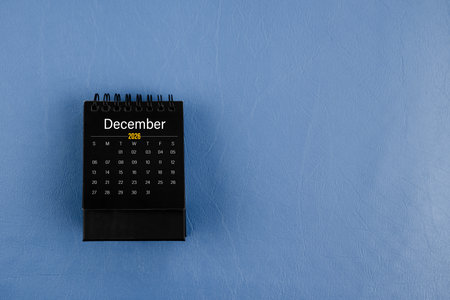December 2026 black desk calendar on navy blue leather background.
