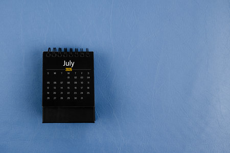 July 2026 black desk calendar on navy blue leather background.