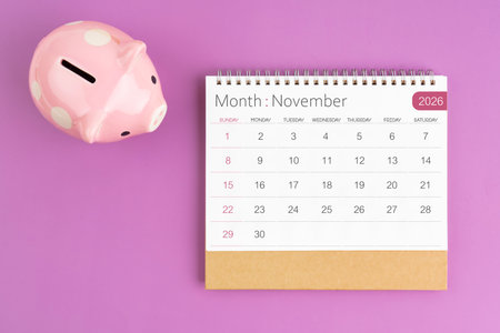 November 2026 desk calendar and pink piggy bank on purple color background.の写真素材