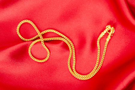 Gold chain necklace on red color silk textile.