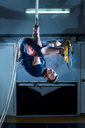Yong athlete is hanging on the rope in gymの写真素材