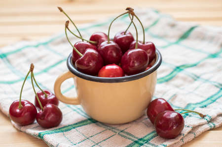 Red cherries in the yellow cup and on the wooden table with tablecloth