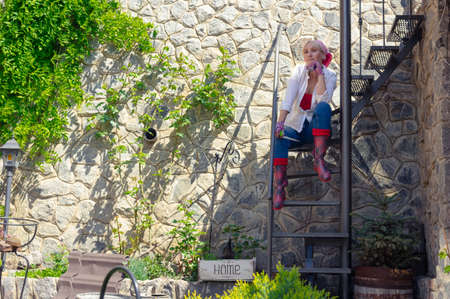 Blond middle aged woman is resting on the spiral stairs of her backyardの写真素材