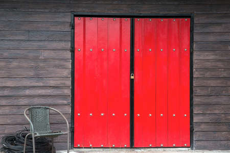Red door  and Brown wooden wall with wicker chair in front of the door.の写真素材