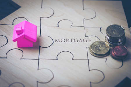 The house and coins are placed on a piece of puzzles with last piece with text mortgage. concept...