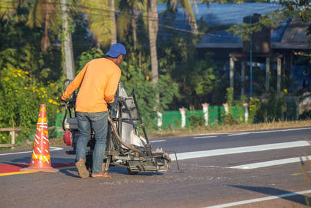 Thermoplastic spray marking machine during road construction. Worker painting white line on the street surface (Road worker painting)の写真素材