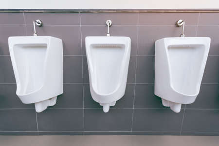 Men's room with white porcelain urinals in line. Modern clean public toilets with tiles . Comfort male toilet urinal concept.の写真素材