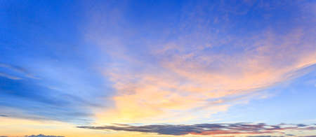 Wide panorama of sunset sky with clouds and sunlight over the sea for your idea of web header. Cloudy landscape for background in serenity colors - blue, ultra violet, yellow and pink tone.の写真素材