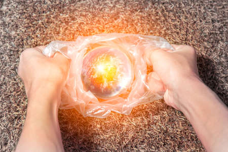The concept of World Environment Day. The man's hand holds the earth in a plastic bag. Dead grassland background Global warmingの写真素材
