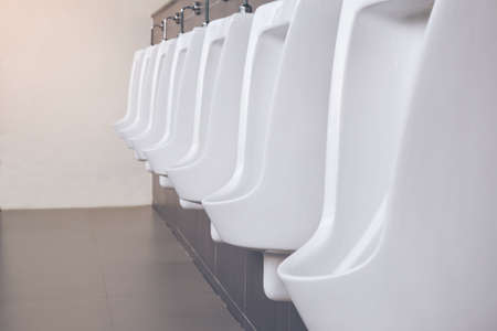 Men's room with white porcelain urinals in line. Modern clean public toilets with tiles . Comfort male toilet urinal concept.の写真素材