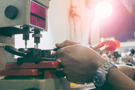 Locksmith in workshop makes new key. Professional making key in locksmith. Machine production of duplicate metal key.の写真素材