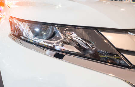 White car, outdoors. Predatory car headlight and hood of powerful sports car with matte White.