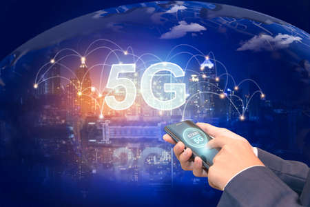 Creative background, male hand holding a phone with a 5G hologram on the background of the city. The...