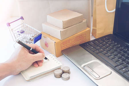 Side view. Young business sitting at table and taking notes in notebook. Student learning online. Blogger.の写真素材