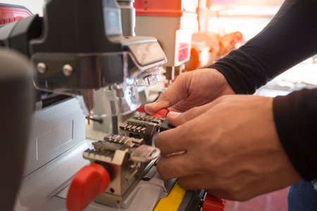 Locksmith in workshop makes new key. Professional making key in locksmith. Machine production of duplicate metal key.の写真素材