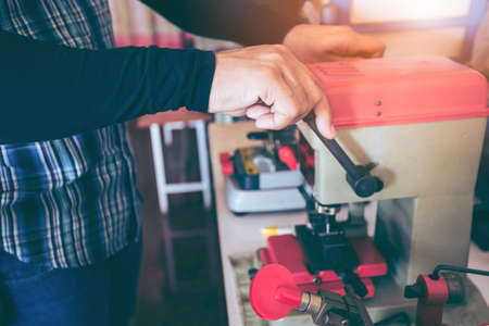 Locksmith in workshop makes new key. Professional making key in locksmith. Machine production of duplicate metal key.の写真素材