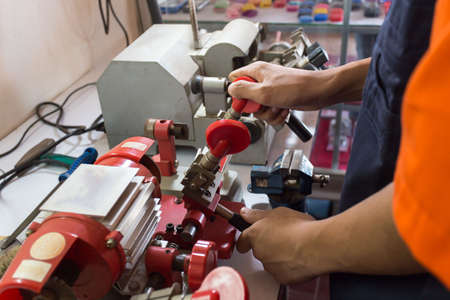 Locksmith in workshop makes new key. Professional making key in locksmith. Machine production of duplicate metal key.の写真素材