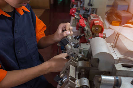 Locksmith in workshop makes new key. Professional making key in locksmith. Machine production of duplicate metal key.の写真素材