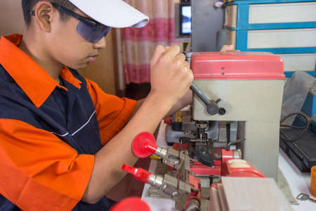 Locksmith in workshop makes new key. Professional making key in locksmith. Machine production of duplicate metal key.の写真素材