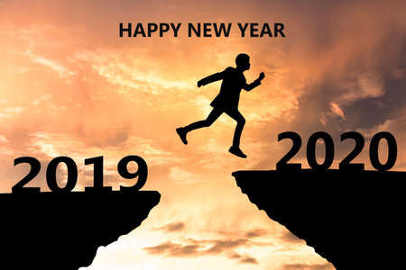 Happy New Year 2020 Silhouette. Young man jumps over a cliff in 2019 to a cliff in 2020. Sunset timeの写真素材