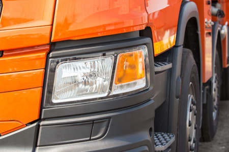 detail of a truck. A fragment of a large commercial semi truck with modern design of headlights,  a shining bumper and a orange lacquered paint finish with glareの写真素材