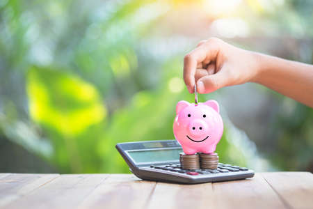 Piggy bank is placed on the calculator. hand that is coin down the piggy bank. planning savings money of coins to buy a home concept for property, mortgage and real estate investment.to buy a house.の写真素材