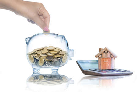 House is placed on the calculator. hand that is coin down the piggy bank isolated on White. planning savings money of coins to buy a home concept for property, mortgage and real estate investment.の写真素材