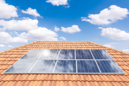 Solar panel on a red roof reflecting the sun and the cloudless blue skyの写真素材