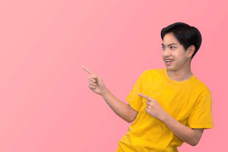Side view portrait of smiling young handsome Asian man pointing fingers in empty space aside in isolated studio pink backgroundの写真素材