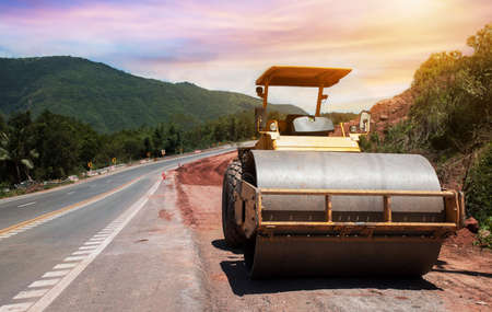 Roller rolling fresh hot asphalt on the new road. Road construction. Road roller at road construction site with cloudy blue sky during sunsetの写真素材