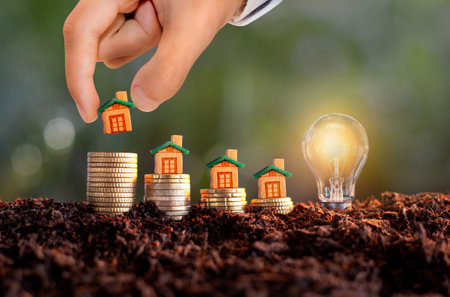 Man hand placing house model on stack of coins, Real estate or property development. Creative light bulb idea, power energy or business idea concept ecology, loan, mortgage, property or home.の写真素材