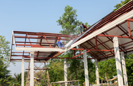 Roof repair, Construction worker installing new roof, roofing tools, power drill used on new roof with sheet metal. Roofing - construction worker standing on a roof covering it with metal.の写真素材