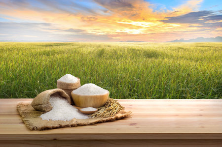 Asian uncooked white rice with the sunset rice field background and burlap sack on wooden table. rice grains healthy foodの写真素材