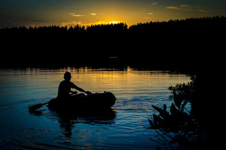 A fisherman floating on a boat on the lake at sunsetの写真素材
