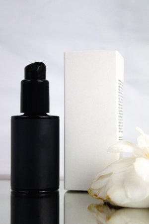 Product photo of black bottle and white box of natural cosmetics, on a white background with camellia flower, vertical photo, for mockupsの写真素材