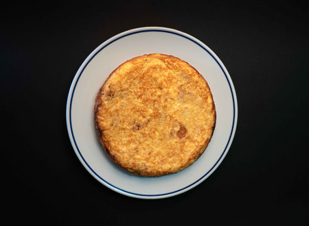 A classic Spanish potato omelette, known as 'tortilla de patatas,' elegantly served in an omelette restaurant against a striking black background. This traditional dish features a hearty combination of potatoes and eggs, skillfully prepared to perfectionの写真素材