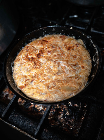 Experience the authentic charm of Spanish cuisine as a traditional potato omelette sizzles on the iron stove. The crackling sound and aroma fill the rustic kitchen, transporting you to the heart of culinary delight. Join us on this culinary journey and savor the essence of homemade cookingの写真素材