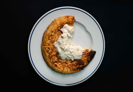 Experience a delightful blend of Spanish tradition and Italian flair with our savory potato omelet, featuring tender potatoes, eggs, and a luscious carbonara sauce. Served on a pristine white plate against a striking black backdrop, it's the perfect appetizer for your culinary journeyの写真素材