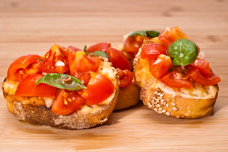 Fresh homemade crispy Italian appetizer called Bruschetta topped with tomato, garlic and basil on wooden boardの写真素材