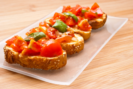 Fresh homemade crispy Italian appetizer called Bruschetta topped with tomato, garlic and basil on wooden boardの写真素材