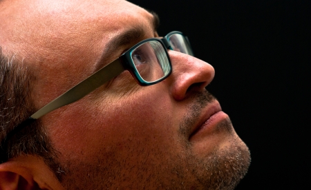 Horizontal closeup of bearded caucasian man wearing glasses looking up on black