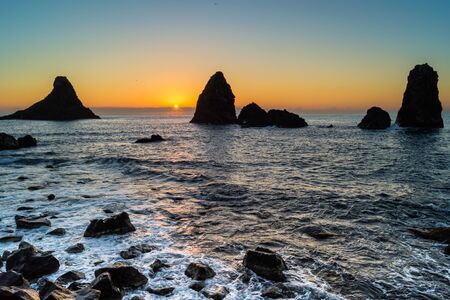 Dawn in the bay of Acitrezza, Sicily, with a silhouette view of its typical lava stacks (Faraglioni).の写真素材
