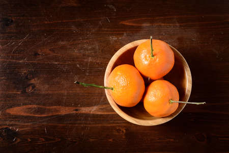 tangerine in a  wooden bowl on dark wooden tableの写真素材