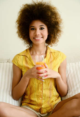 beautiful smiling girl drinking orange juice at homeの写真素材